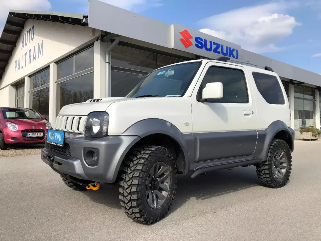 weißer Suzuki vor Autohaus mit rotem Suzuki im Hintergrund